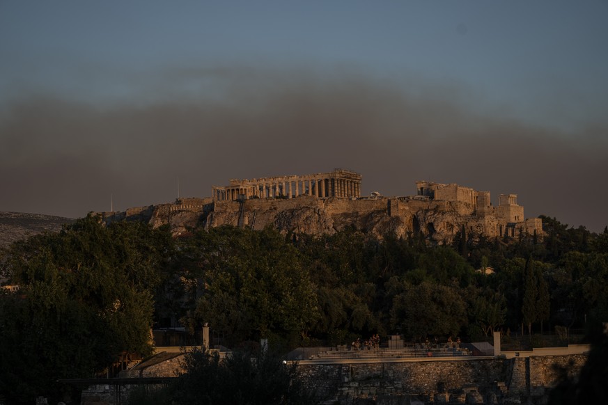 Smoke from a fire blanketed part of the Athenian sky as it is seen behind the ancient Acropolis hill with the Parthenon temple on Tuesday, July 19, 2022. In Greece, hundreds of people were ordered to  ...