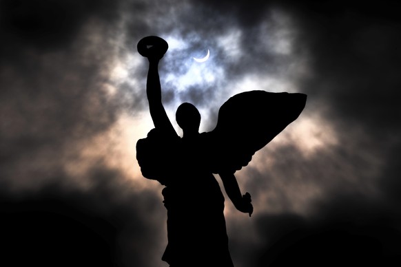 The moon makes its way in front of the sun during a total solar eclipse framed above the angel atop the Princes&#039; Gates, in Toronto, Monday, April 8, 2024. (Frank Gunn/The Canadian Press via AP)