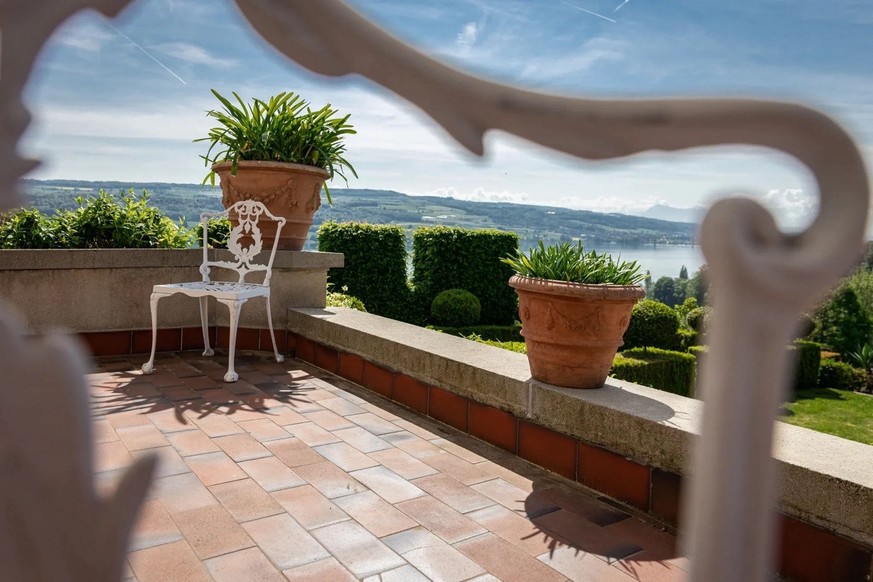 Une terrasse à l'air méditerranéen avec des grands pots en terre cuite, un carrelage dans les même tons et une chaise de jardin en fer forgé blanc.