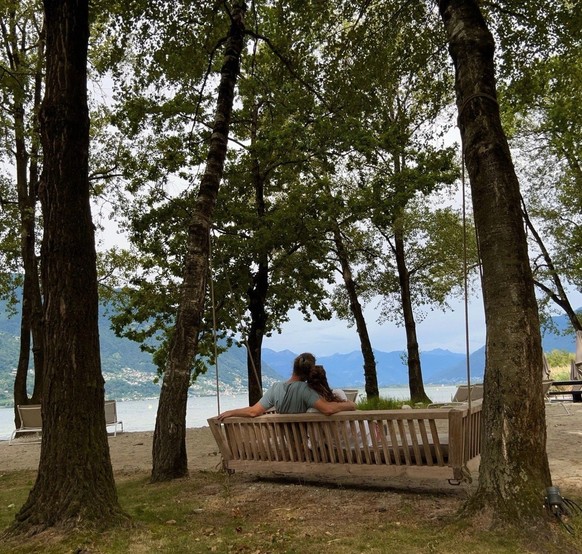 La journaliste Rahel Empl et son mari, photographiés de dos, assis sur un banc en bois, sous les arbres, au Castello del Sole Beach Resort &amp; Spa, à Ascona.