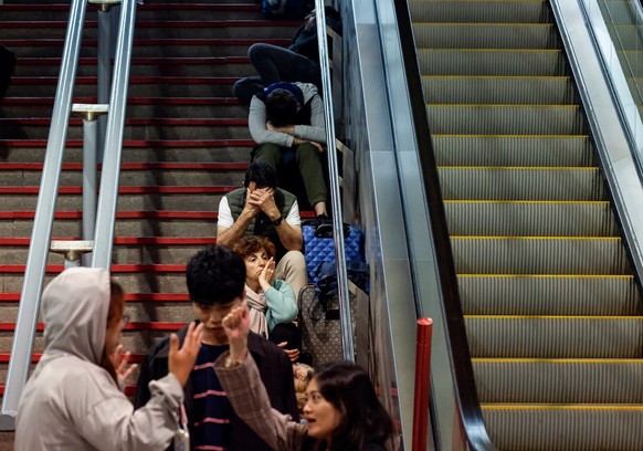 Travelers sit on the stairs as they prepare to spend the night at the Atocha train station, following a massive power cut affecting the entire Iberian peninsula and the south of France, in Madrid on A ...