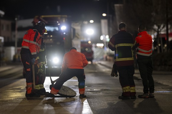 epa12810318 Firefighters lift a drain cover next to the site where a postal bus caught fire in Kerzers, Switzerland, 10 March 2026. According to Fribourg cantonal police, several passengers were kille ...