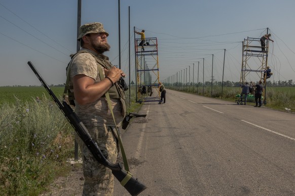 A Ukrainian serviceman stands guard with a shotgun as his fellow soldiers install anti-drone nets over a road at an undisclosed location in the eastern Donetsk region on July 8, 2025, amid the Russian ...