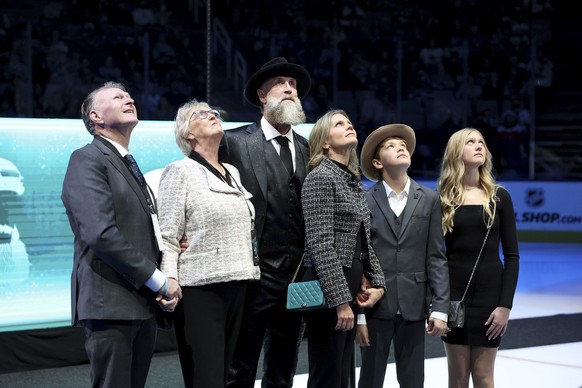 Joe Thornton, standing with his wife Tabea, children River and Ayla, and parents Wayne and Mary Thornton, watches a highlight video of his career during a ceremony to retire his jersey before an NHL H ...