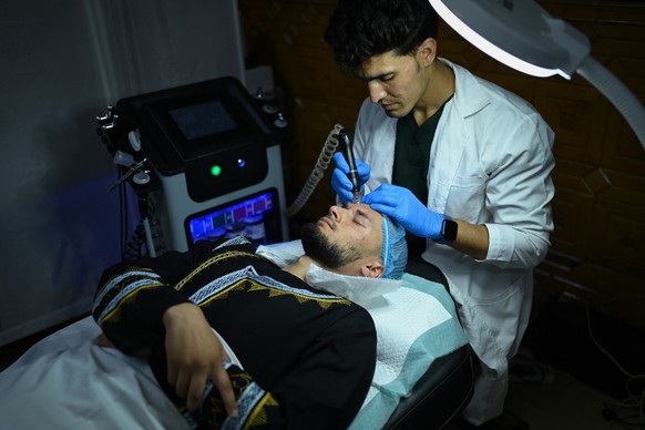 In this photograph taken on August 13, 2025, a member of the medical staff performs hydrafacial on an Afghan man at a beauty clinic in Kabul. Decked with fake crystal chandeliers and velvet sofas, cos ...
