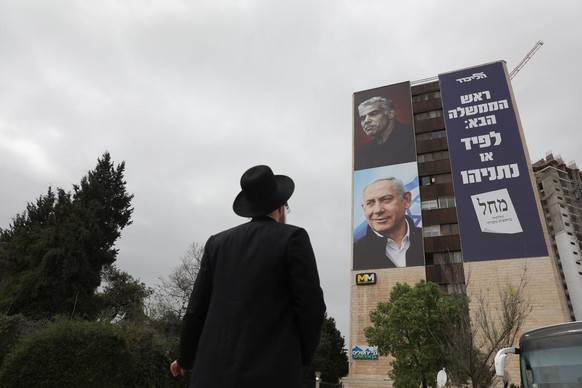 epa09089576 An Ultra orthodox Jewish man looks on elections billboard showing Israeli prime minister Benjamin Netanyahu with his political rival Yair Lapid in Jerusalem, Israel, 22 March 2021. Israel  ...