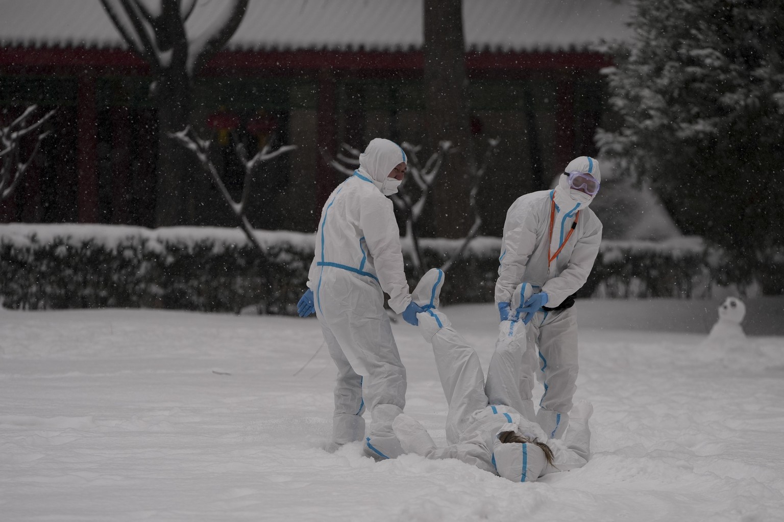 Workers wearing protective suits play outside with snow at the 2022 Winter Olympics, Sunday, Feb. 13, 2022, in Beijing. (AP Photo/Natacha Pisarenko)