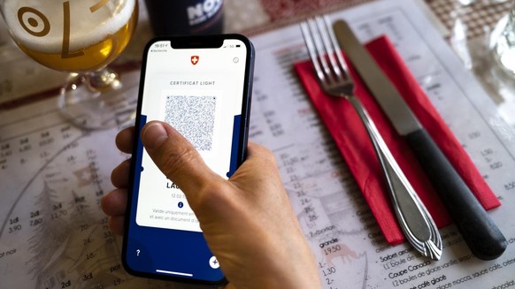 Une personne tient dans sa main un smartphone avec l&#039;application Certifact Covid suisse et un certificat light dans un restaurant ce vendredi 10 septembre 2021 a Rances dans le canton de Vaud. De ...