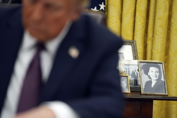 Family photos are seen in the background as President Donald Trump signs executive orders in the Oval Office of the White House, Monday, Jan. 20, 2025, in Washington. (AP Photo/Evan Vucci)