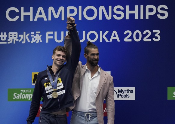 epa10764530 Michael Phelps (R) raises the hand of gold medalist Leon Marchand (L) of France during the awarding ceremony of the Men&#039;s 400m Individual Medley final of the Swimming events during th ...