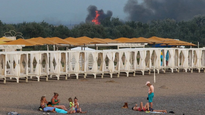 Des gens sont allongés sur la plage en Crimée : en arrière-plan, des explosions retentissent dans une base militaire russe.