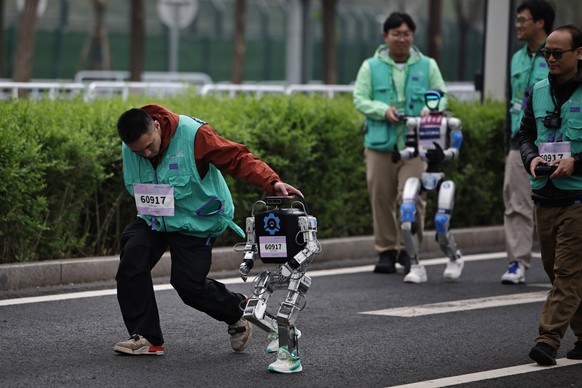 epa12040342 Teams accompany humanoid robots during a half marathon run by humans and robots in Beijing, China, 19 April 2025. China hosts the world?s first all-robot marathon in Beijing, showcasing th ...