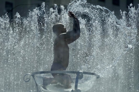 A man sits in a glas bowl in a fountain on the Southbank in London, Tuesday, July 19, 2022. Millions of people in Britain woke from the country's warmest-ever night on Tuesday and braced for a da ...