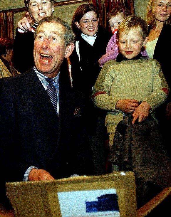 LONDON - DECEMBER 11: Prince Charles, with help from 7-year-old Jack Holt, unwraps a gift of gold leaves, part of a decorative stone pear and apple, at a reception for children suffering from cancer a ...
