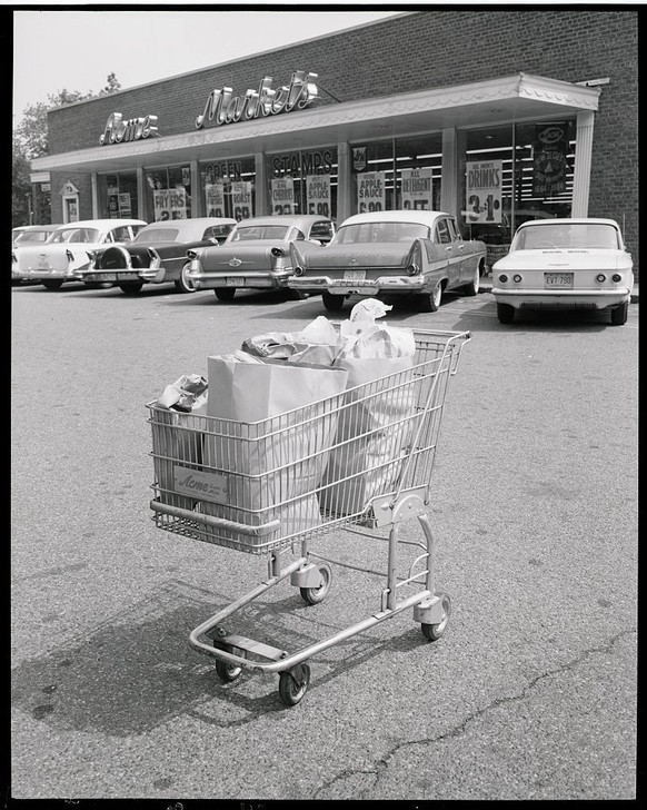 (Original Caption) Still life photo of a full shopping cart in a supermarket parking lot. SEE NOTE