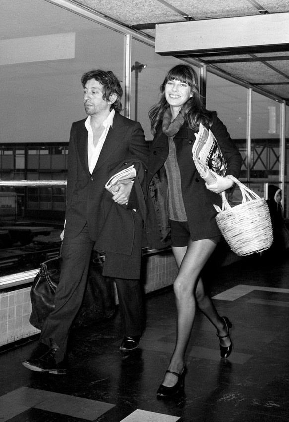 Jane Birkin et Serge Gainsbourg à l’aéroport d’Heathrow à Londres, qui transporte, en guise de bagage, un sac Haut à Courroies signé Hermès.