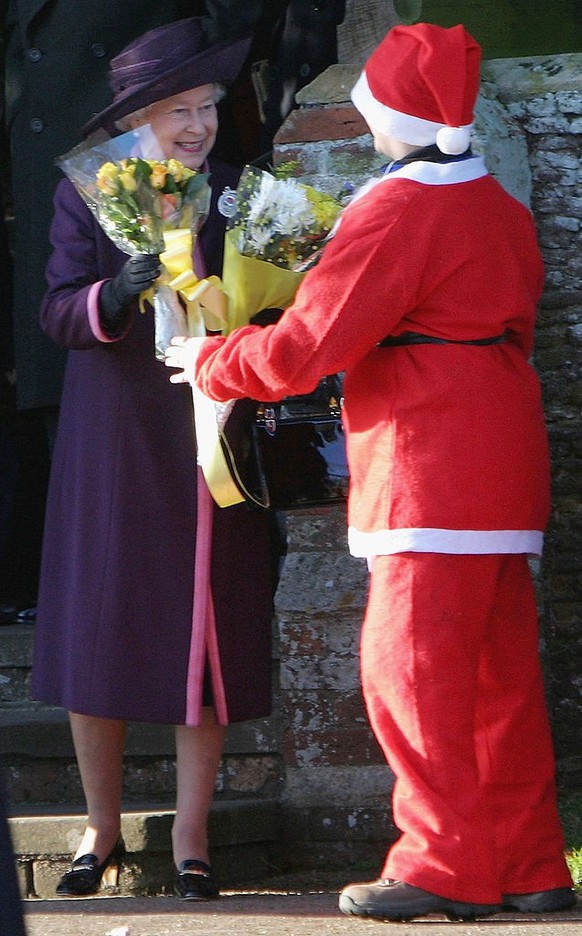 SANDRINGHAM, ENGLAND - DECEMBER 25: Britain&#039;s Queen Elizabeth II accepts a bunch of flower from a boy dresses as Father Christmas after she attended the Christmas Day service at Sandringham Churc ...