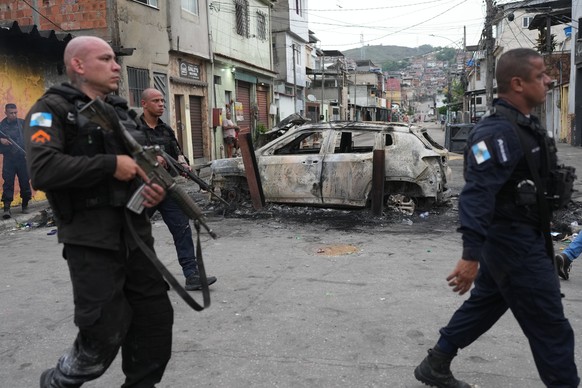 Police walk past a burned car used by alleged drug traffickers as a roadblock during a police operation in the Complexo do Alemao favela where the criminal organization &quot;Comando Vermelho&quot; op ...