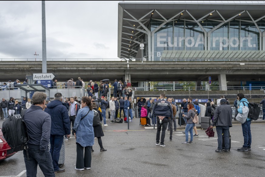 Menschen warten mit ihrem Gepaeck vor dem evakuierten Flughafen Euroairport Basel-Muelhausen am Freitag, 20. Oktober 2023. Der Flughafen ist am fruehen Freitagnachmittag wegen eines Bombenalarms erneu ...
