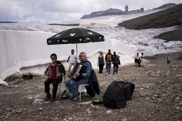 epa10108828 Two people play accordions to encourage the participants next to blanket covering snow from the last winter season to prevent it from melting, next to the Tsanfleuron glacier approaching t ...