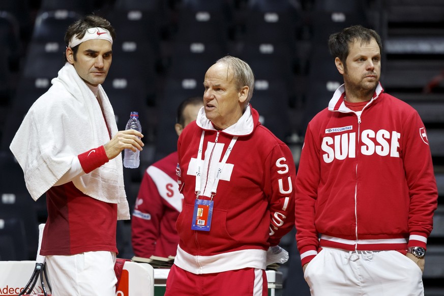 Swiss doctor Roland Biedert, centre, speaks with Roger Federer, left, of Switzerland, next to Swiss Davis Cup Team captain Severin Luethi, right, during a training session of the Swiss Davis Cup Team, ...