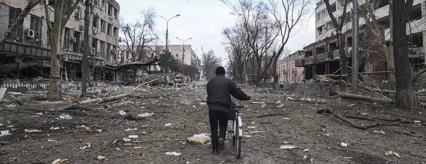 FILE - A man walks with a bicycle in a street damaged by shelling in Mariupol, Ukraine, March 10, 2022. In talks between Russia and Ukraine toward a possible cease-fire after three weeks of intense fi ...