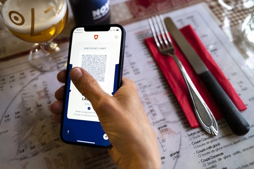 Une personne tient dans sa main un smartphone avec l&#039;application Certifact Covid suisse et un certificat light dans un restaurant ce vendredi 10 septembre 2021 a Rances dans le canton de Vaud. De ...