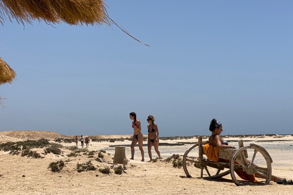 (FILES) Tourists walk by as a woman sits on a bench at the Ras Hankorab beach in the Red Sea Wadi Al-Gemal protectorate in southern Egypt on May 28, 2025. Wadi al-Gemal National Park, declared a prote ...