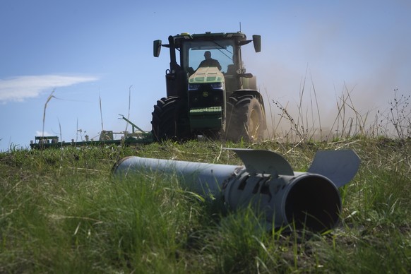 A fragment of a Russian missile is seen in the foreground as a farmer works on his field in Izium, Kharkiv region, Ukraine, Saturday, Apr. 20, 2024. (AP Photo/Andrii Marienko)