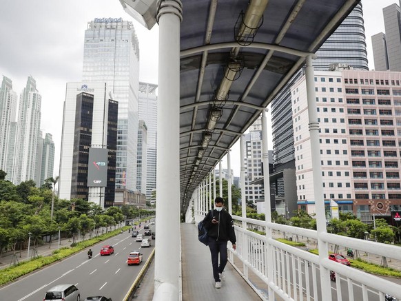 epa08919714 A man wearing a protective face mask walks on a pedestrian bridge at a business area in Jakarta, Indonesia, 05 January 2021. The country&#039;s inflation rate through 2020 recorded at 1.68 ...