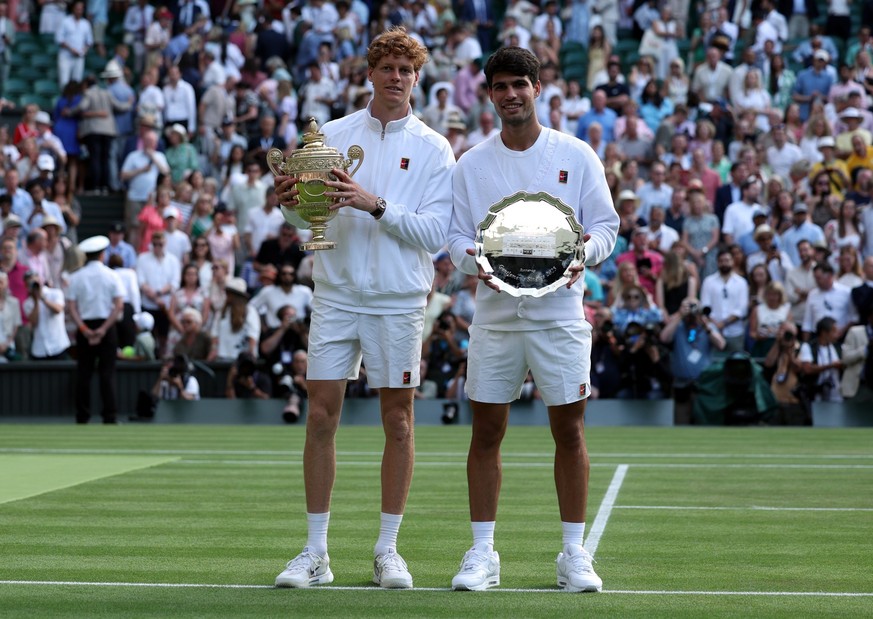 epa12236326 Jannik Sinner of Italy (L) celebrates with the trophy after winning the Men's Singles final match against Carlos Alcaraz of Spain (R) with his runner-up trophy at the Wimbledon Champi ...