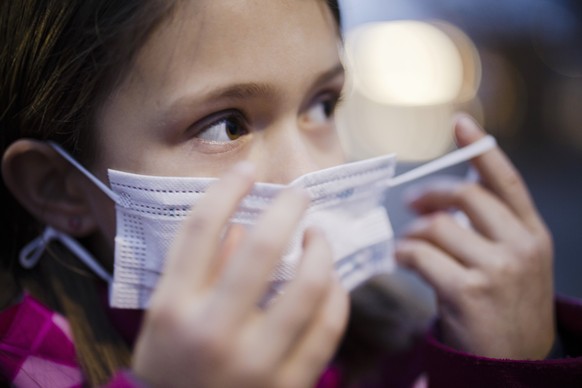 Eine Primarschuelerin zieht eine Kinder Maske auf einem Pausenplatz einer Schule an, aufgenommen am Montag, 3. Januar 2022 in Zuerich. Die Maskentragpflicht im Kanton Zuerich wird mit dem Schulstart n ...