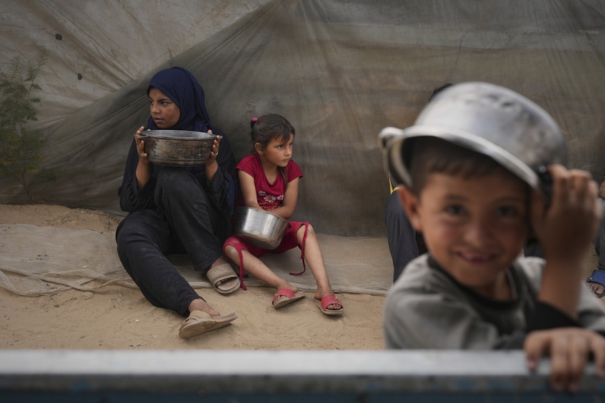 Raghad and her younger sister Mira hold on to their cooking pots as they wait to fill them with food, in Muwasi, on the outskirts of Khan Younis, in the southern Gaza Strip, April 24, 2025. (AP Photo/ ...
