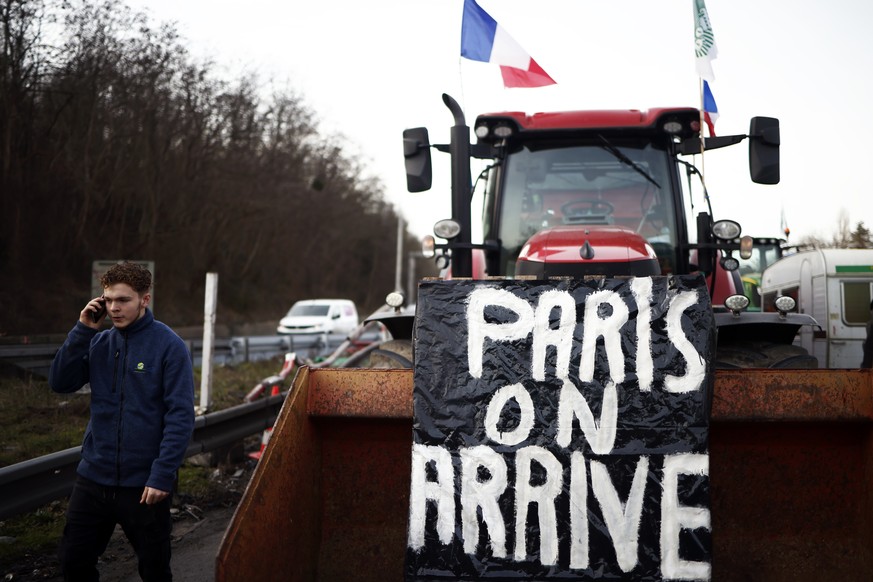 epa11112772 A man walks next to a tractor with the message &#039;Paris we arrive&#039; at the blocking point of the A15 motorway at Argenteuil, north of Paris, France, 29 January 2024. French farmers  ...