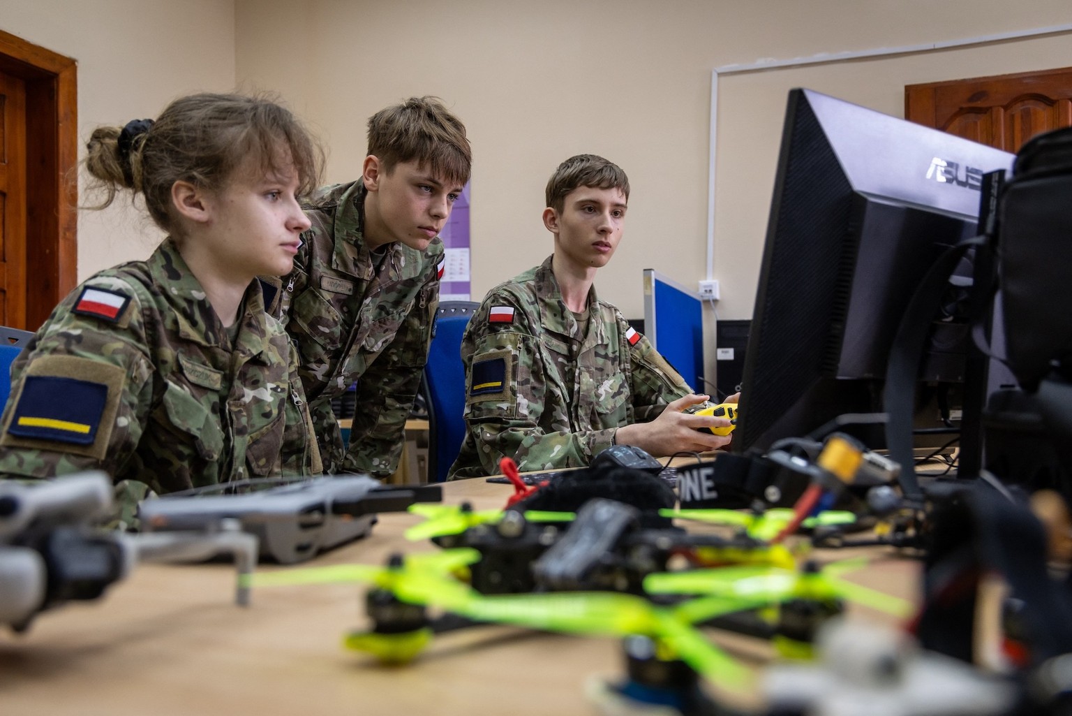 Students of the drone course of the Legnica Military School Aleksandra Kaszczuk (L) and Bartosz Ladocha (C) look on as Tomasz Cieslak (R) flies a drone simulator in the computer classroom of the schoo ...