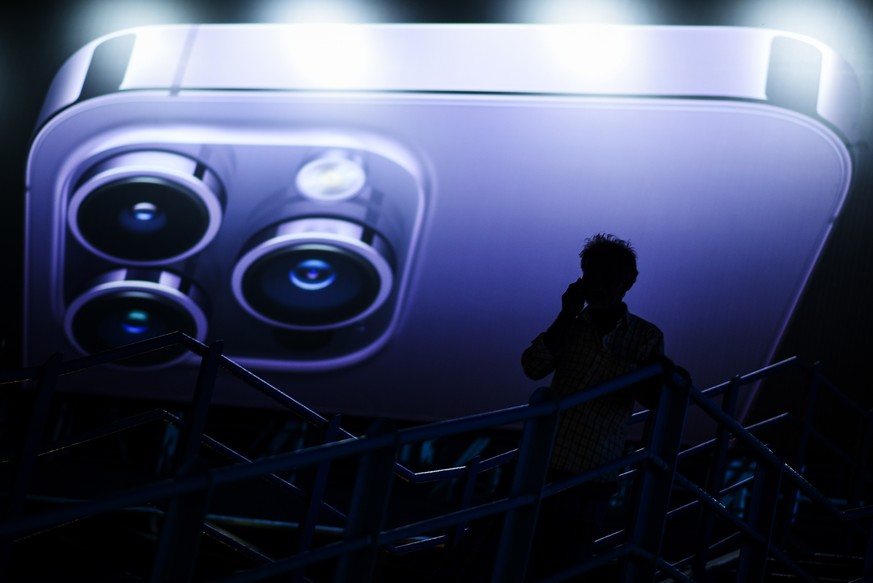 epa10180004 A man speaks on a mobile phone as he walks down a pedestrian bridge while passing in front of an Apple iPhone 14 advertisement billboard, in Chennai, India, 12 September 2022. Tata Group i ...