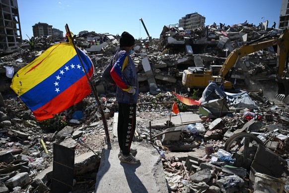 A man stands next to a Venezuelan flag as a backhoe loader removes debris in Caraballeda, La Guaira state, Venezuela, on July 7, 2026, following earthquakes that struck the region. The death toll from ...