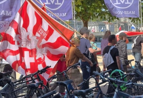 Ivan G.* brandissant un drapeau suisse à flammes. A sa droite, Eneas W.* coiffé d’une casquette noire.