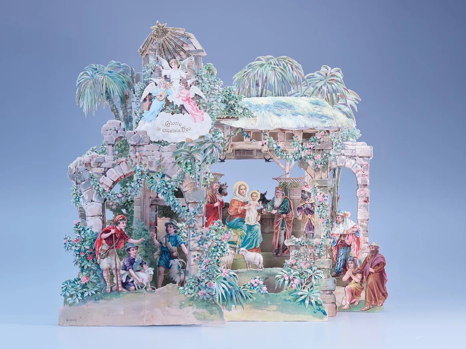 Dans cette crèche pliable, la Sainte Famille est entourée d’une construction en pierre partiellement délabrée, envahie de palmiers et de plantes grimpantes en fleurs. Réalisée en papier et en carton v ...