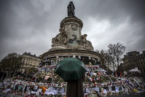 epa05040515 A pedestrian with an umbrella pauses in front of the memorial of candles and flowers for the victims of the 13 November Paris attacks, on Place de la Republique in Paris, France, 24 Novemb ...