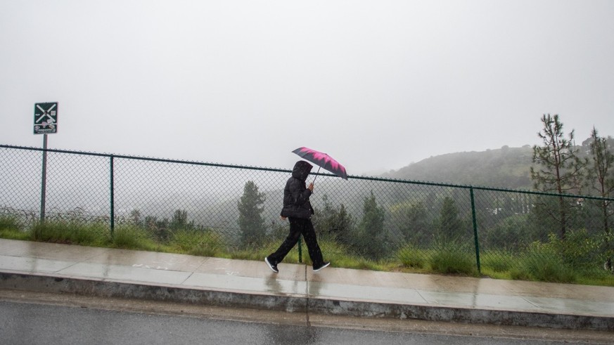 A tourist walks on the rain near the Hollywood sign that has the view blocked by clouds and heavy rain on December 24, 2025 in Los Angeles, California. A major winter storm rolled into California on D ...