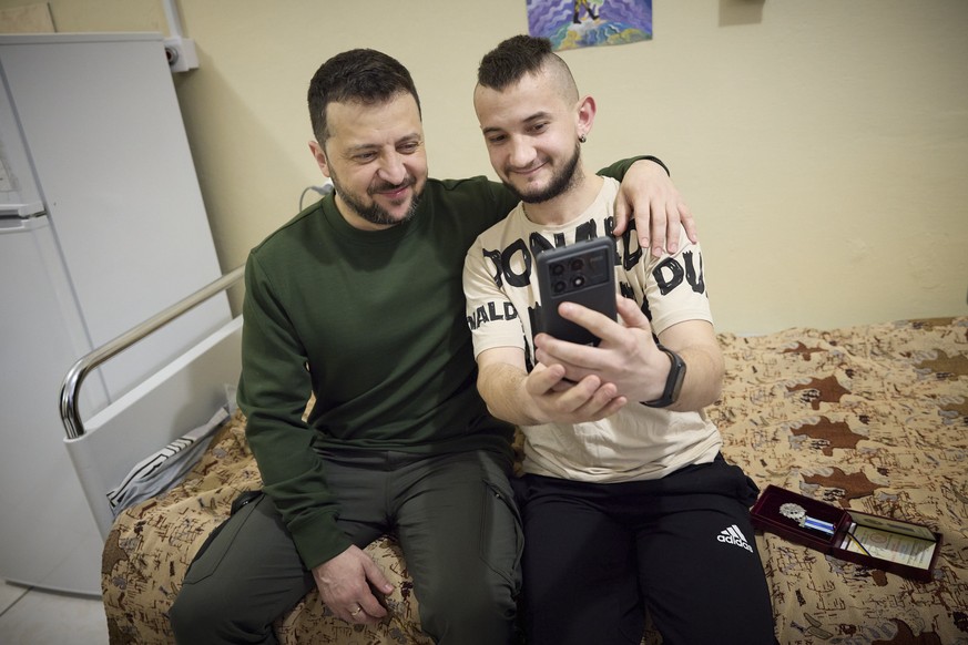 epa11247107 A handout picture made available by the Presidential Press Service shows Ukrainian President Volodymyr Zelensky (L) posing for a selfie with a wounded serviceman at a military hospital dur ...