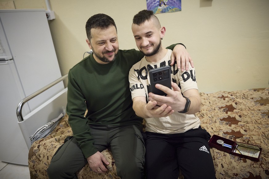 epa11247107 A handout picture made available by the Presidential Press Service shows Ukrainian President Volodymyr Zelensky (L) posing for a selfie with a wounded serviceman at a military hospital dur ...