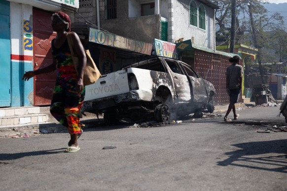 PORT-AU-PRINCE, HAITI- MARCH 07: Citizens pass a burned car as Haiti&#039;s government extended on Thursday the nighttime curfew and state of emergency in the capital of Port-au-Prince for a month ami ...
