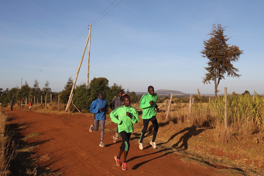 ITEN, KENYA - FEBRUARY 05: Mary Keitany of Kenya and winner of the 2011 London Marathon leads in front of her husband and coach Charles Koech (R) during a training run on February 5, 2012 in Iten, Ken ...