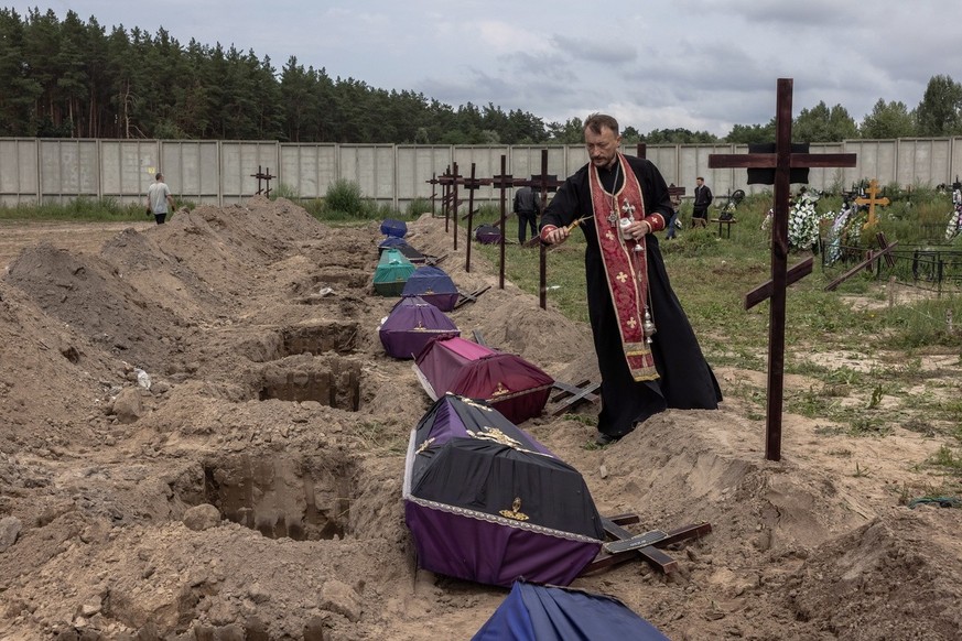 epa10115767 Orthodox priest Andrii Halavin blesses the remains of unidentified people who were killed in the Bucha district at the time of the Russian occupation, during the mass burial at a cemetery  ...