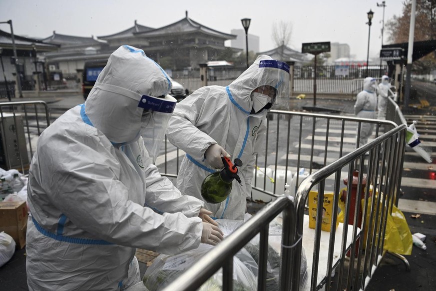 In this photo released by Xinhua News Agency, workers wearing protective suits disinfect packed vegetables at a residential area under quarantine in Xi&#039;an in northwestern China&#039;s Shaanxi Pro ...