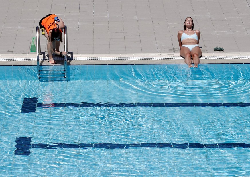 epa08502168 A lifeguard cleans the pool stairs handlers as a woman sunbathes at the public swimming pool in Aranzadi, Pamplona, Spain, 22 June 2020. Public swimming pools reopen to public in the city  ...