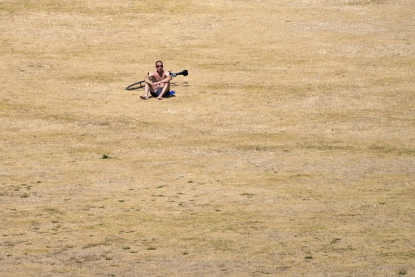 A cyclist sits on the dry grass of Greenwich Park, in south east London, Monday July 18, 2022. Britain���s first-ever extreme heat warning is in effect for large parts of England as authorities prepar ...