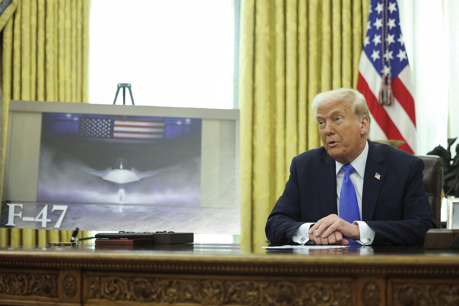 President Donald Trump speaks as an image of an F-47 sixth-generation fighter jet is displayed during an event in the Oval Office of the White House in Washington, Friday, March 21, 2025. (Pool via AP ...